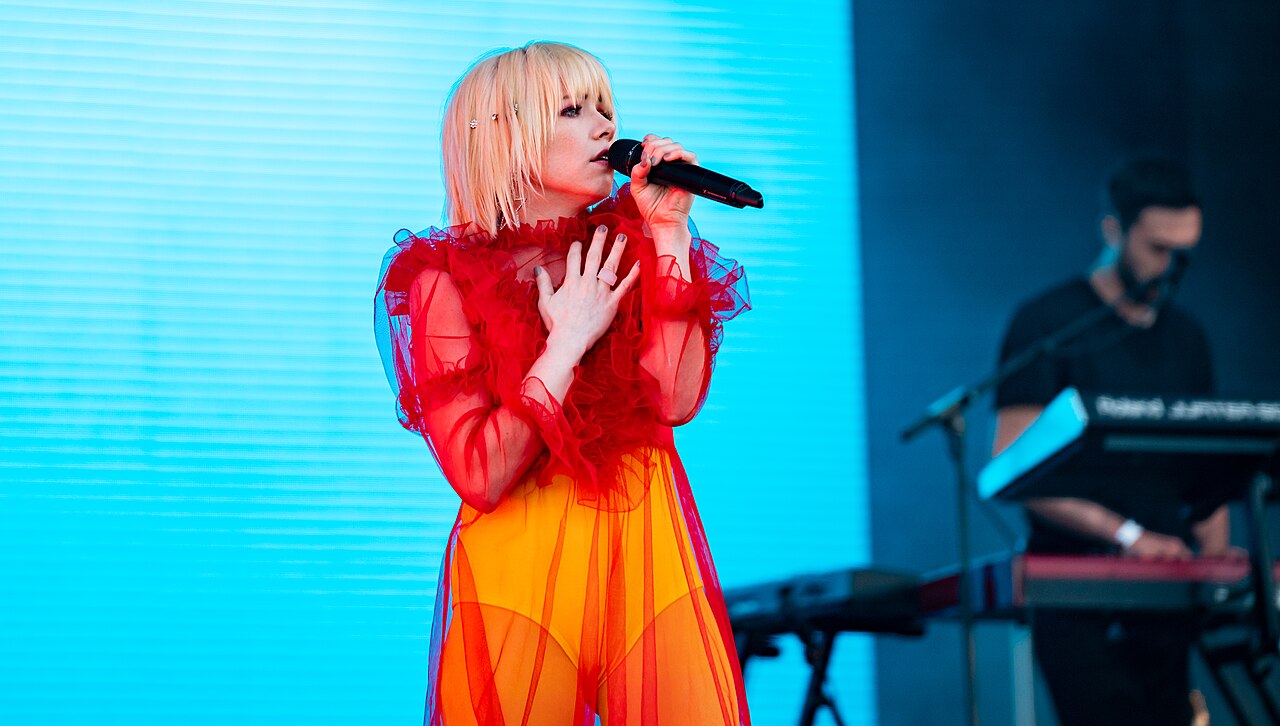 Carly Rae Jepsen canta en un escenario con vestido rojo y fondo azul