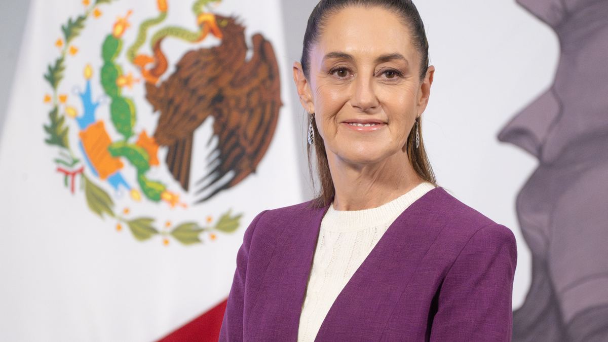 Claudia Sheinbaum durante una conferencia, con la bandera de México al fondo