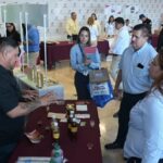 Hecho en Tamaulipas ofrece asesoría y enlaces de venta Participantes conversan junto a una mesa de productos en una exhibición de Hecho en Tamaulipas.
