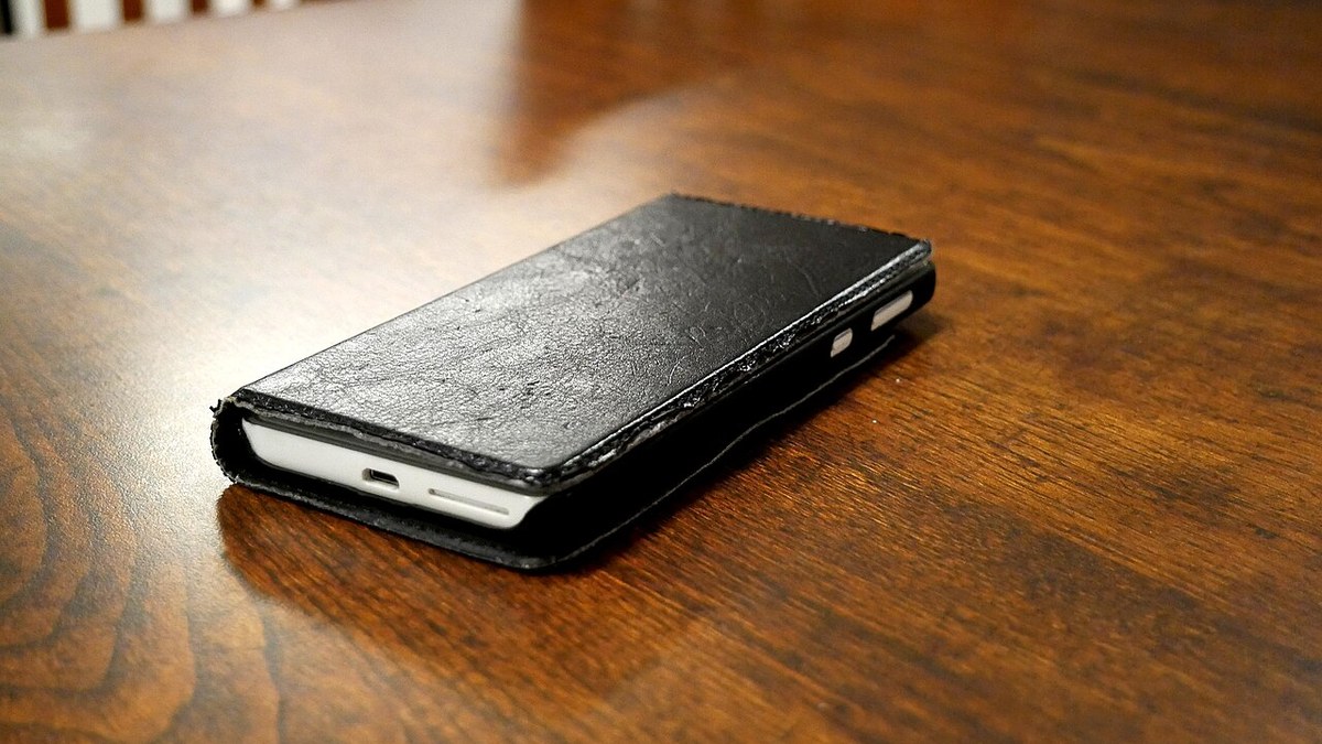 Teléfono móvil con funda negra sobre una mesa de madera; fotografía ilustrativa de archivo, no vinculada con una denuncia.